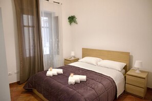 Ein Hotelzimmer mit einem Bett, zwei Nachttischen, einem Vorhangfenster und einer Wandpflanze.