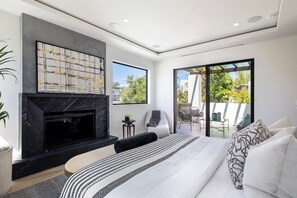 Un dormitorio moderno con chimenea, una cama grande, zona de estar y balcón con mobiliario exterior.