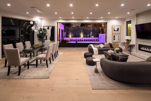 Una sala de estar moderna con comedor, chimenea y vista a un jardín de noche.