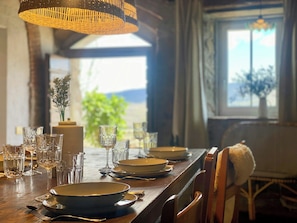 A dining table set with plates, glasses, and cutlery, with a view of greenery and a window in the background. - Medieval house with jacuzzi in Val di Cecina (Castelnuovo di Val di Cecina)