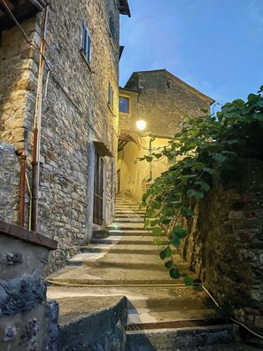 A stone staircase leading to a building with a lit entrance, surrounded by vegetation. - Medieval house with jacuzzi in Val di Cecina (Castelnuovo di Val di Cecina)