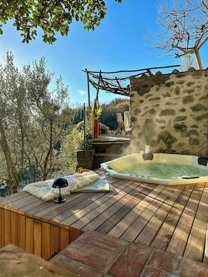 A wooden deck with a hot tub, a stone wall, and a rustic wooden pergola. - Medieval house with jacuzzi in Val di Cecina (Castelnuovo di Val di Cecina)