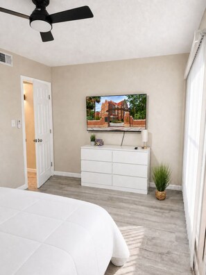 A bedroom with a bed, a ceiling fan, a white dresser, a television on the wall, and a door leading to another room. - Walk to Shands Hospital & UF - Pool (Gainesville)