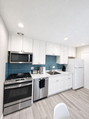 A modern kitchen with white cabinets, stainless steel appliances, a blue tiled backsplash, and a white countertop. - Walk to Shands Hospital & UF - Pool (Gainesville)