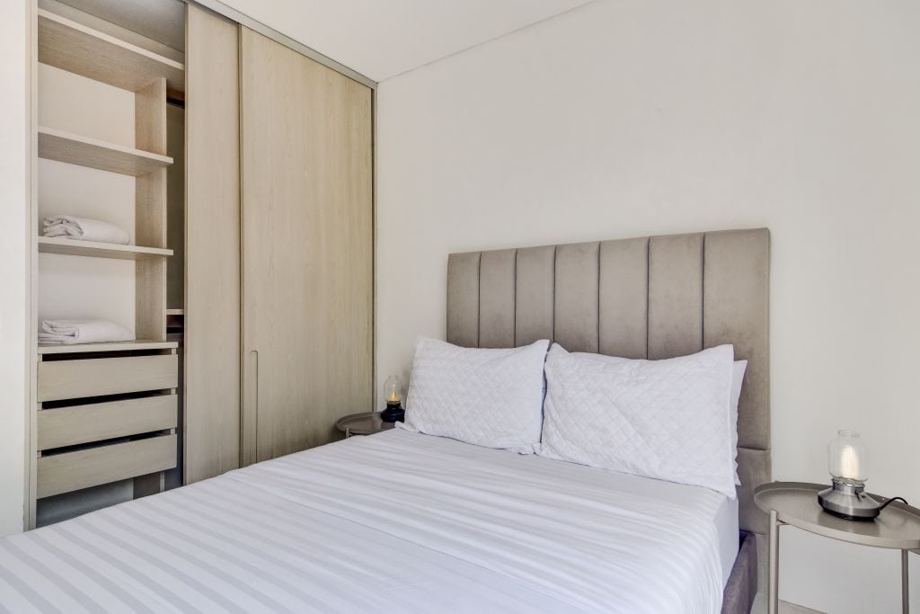 A bedroom with a bed, a nightstand, a bedside lamp, and a wardrobe.