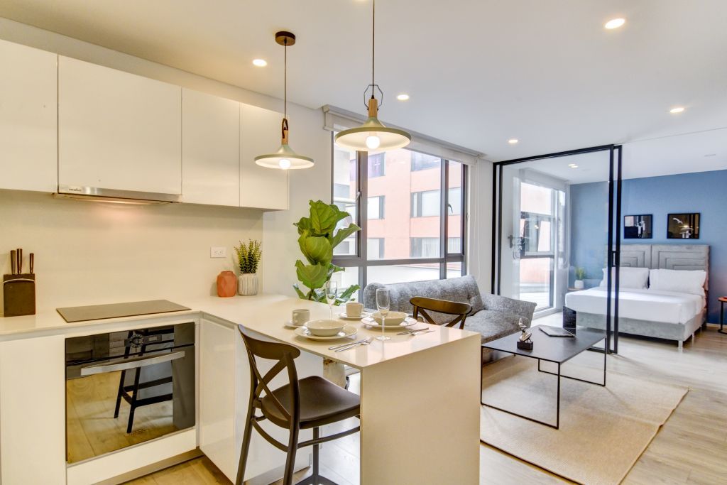 A modern kitchen with a dining area, a sofa, and a bed in the adjacent room.