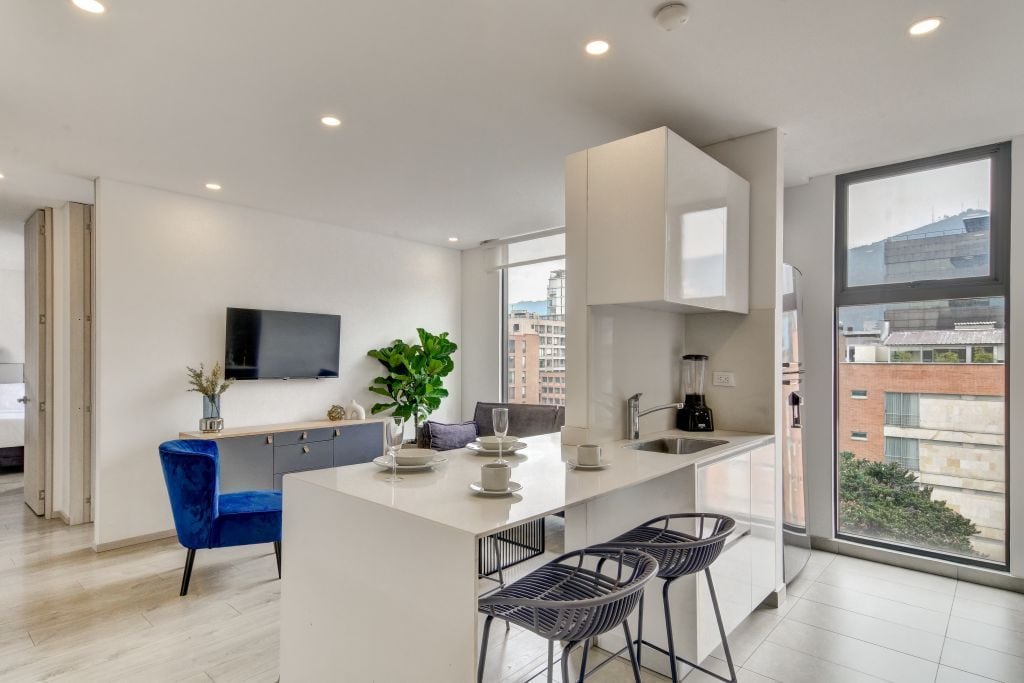 Una cocina moderna con una isla central, taburetes de bar, un televisor de pantalla plana y un amplio ventanal con vistas a la ciudad.