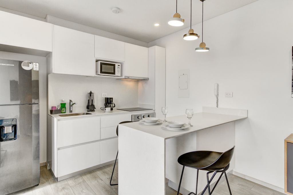 Una cocina moderna con armarios blancos, microondas integrado, cafetera y una barra con taburetes.