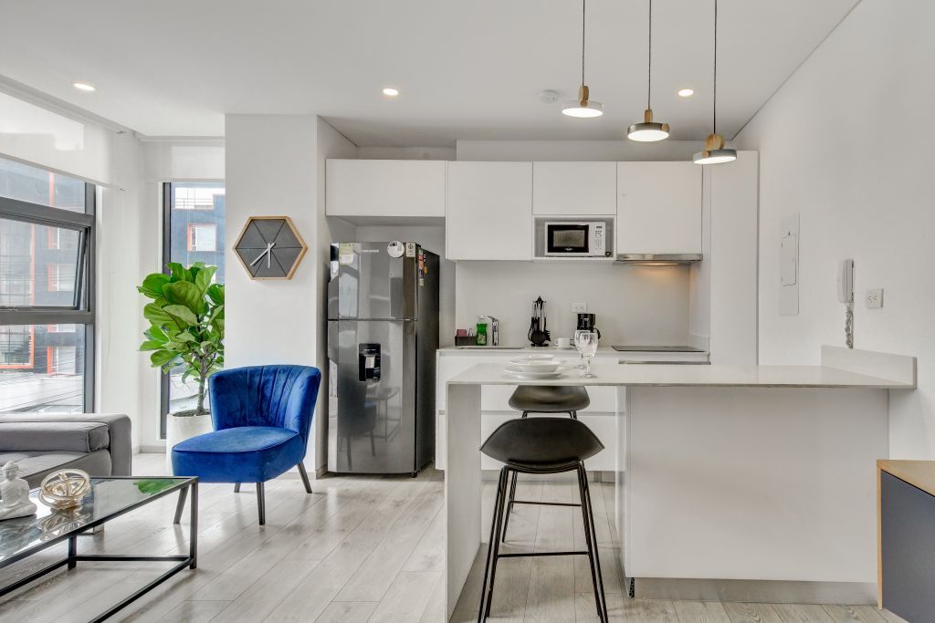 Una cocina moderna con armarios blancos, un refrigerador de acero inoxidable, un microondas y un taburete de bar.