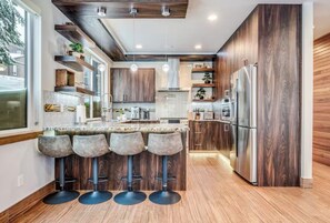 A modern kitchen with wooden cabinets, a stainless steel refrigerator, and a bar area with stools. - Mountain View Estate Entire Cabin in Snoqualmie Pass, 16+ Sauna SteamRoom Hottub (Snoqualmie Pass)