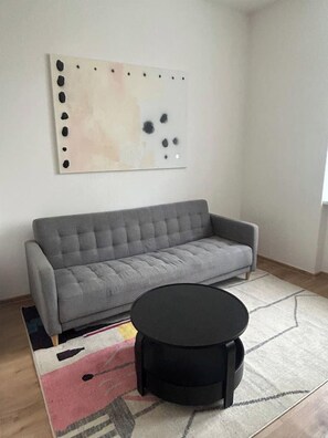 A living room with a gray sofa, a black round coffee table, and a colorful rug. - Minimalist Design Studio (Prague)