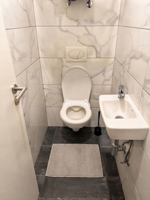 A bathroom with a toilet, sink, and marble walls. - Minimalist Design Studio (Prague)