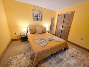 A bedroom with a bed, nightstand, lamp, and a door. - Huckleberry Lodge | Blue Ridge View | Clawfoot Tub (Wythe County)