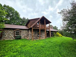 A stone building with a wooden balcony, surrounded by lush green grass and trees. - Huckleberry Lodge | Blue Ridge View | Clawfoot Tub (Wythe County)