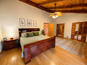 A bedroom with a wooden bed, a nightstand, a ceiling fan, and a large mirror. - Radford Retreat | 3 Min to RDU | Games & Arcade (Radford)