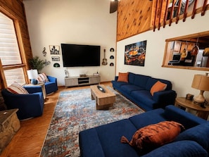 A living room with blue sofas, a coffee table, a flat-screen TV, and a patterned rug. - Radford Retreat | 3 Min to RDU | Games & Arcade (Radford)