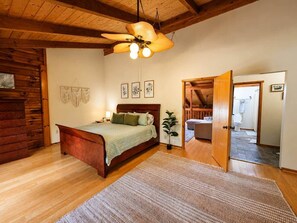 A bedroom with a wooden bed, a ceiling fan, a wall-mounted plant, and a door leading to another room. - Radford Retreat | 3 Min to RDU | Games & Arcade (Radford)