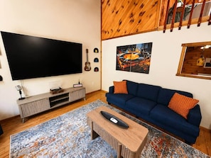 Una sala de estar con un televisor de pantalla plana grande, un sofá azul, una mesa de centro y una alfombra estampada.