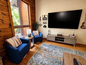A living room with a large TV, two blue sofas, a patterned rug, and a wooden cabinet with a record player. - Radford Retreat | 3 Min to RDU | Games & Arcade (Radford)
