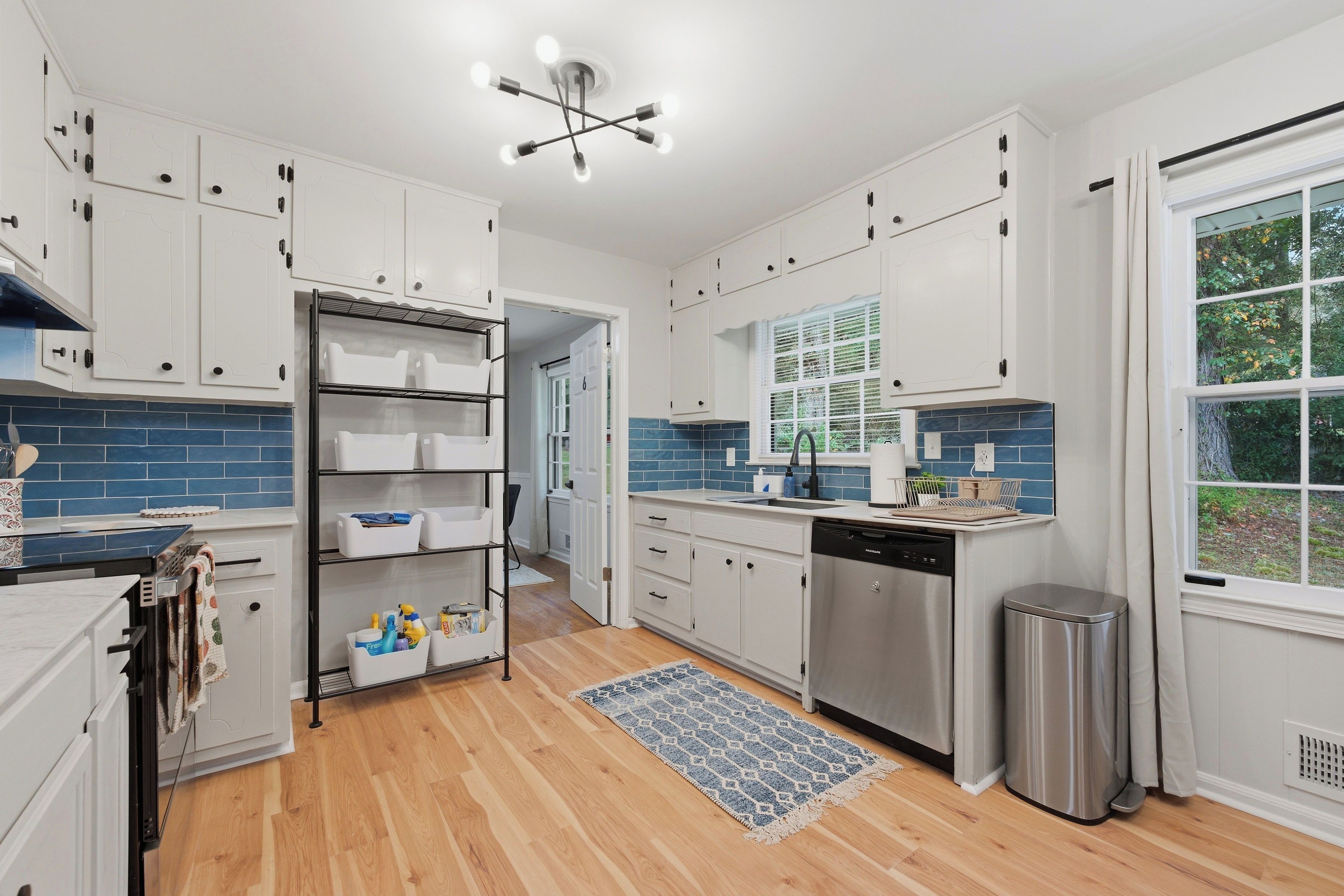 A modern kitchen with white cabinets, a stainless steel dishwasher, and a blue-tiled backsplash.