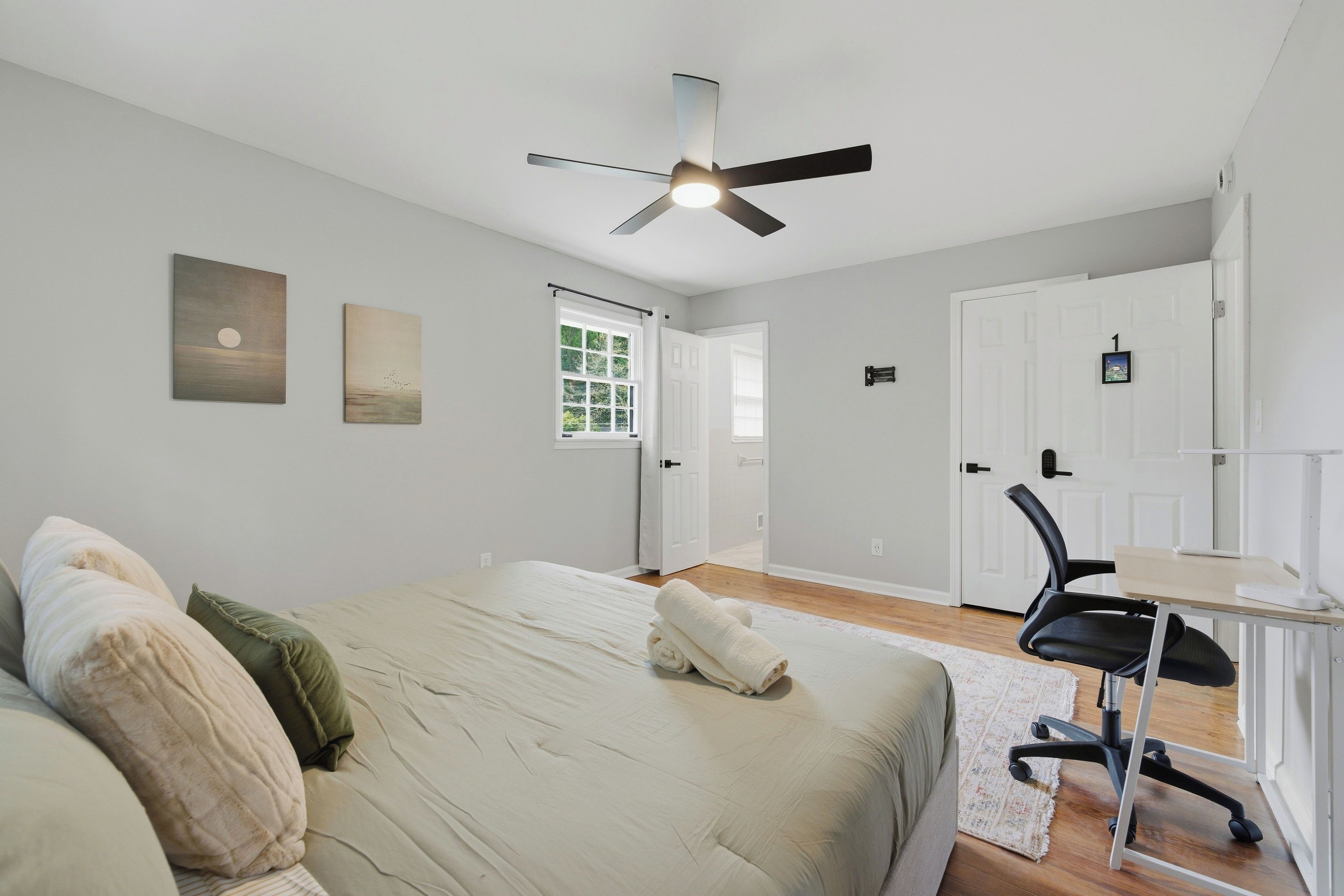 Un dormitorio con cama, escritorio, silla, ventilador de techo y puerta.