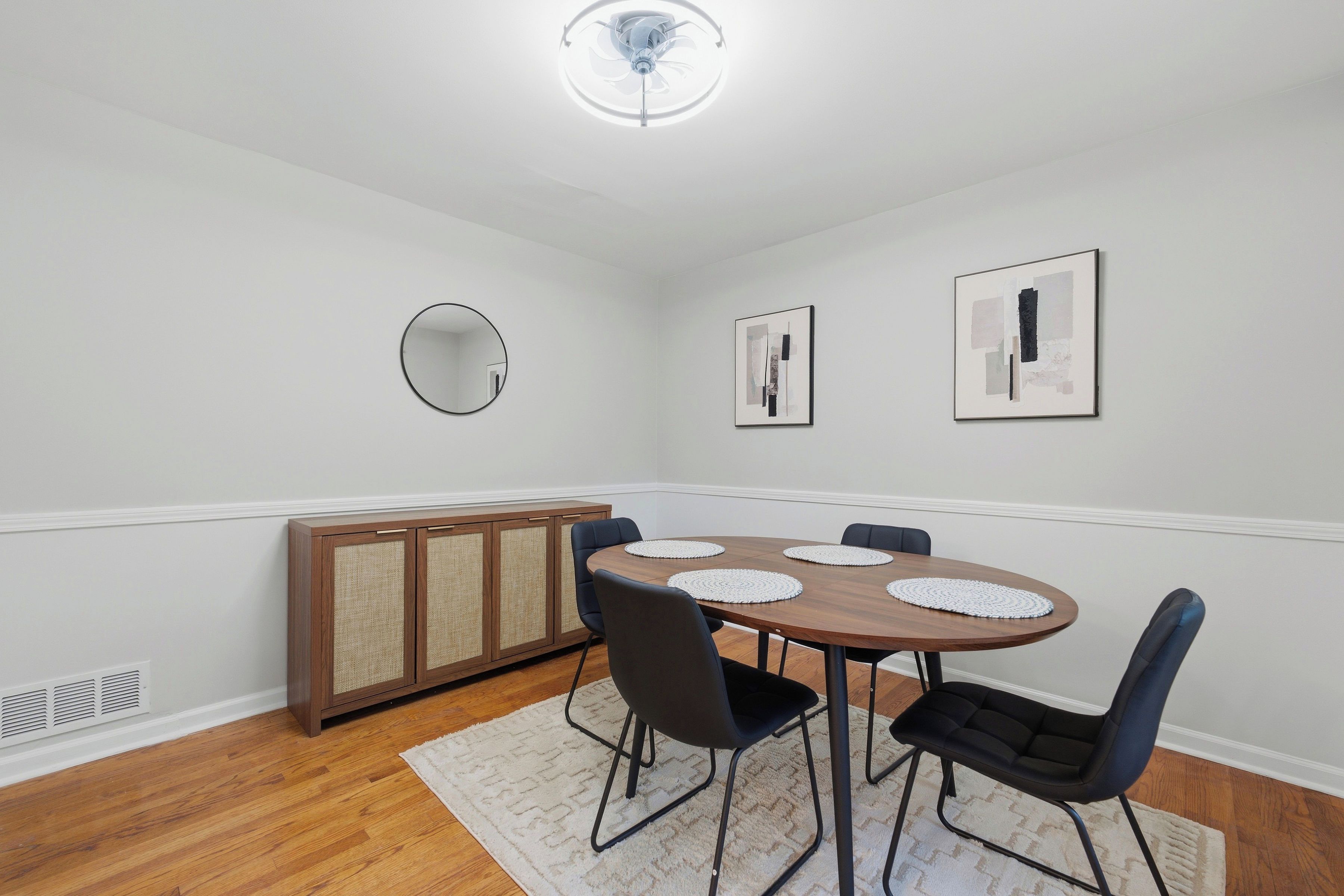 A dining area with a round table, chairs, a cabinet, and wall-mounted artwork.