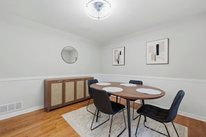 A dining area with a round table, chairs, a cabinet, and wall-mounted artwork. - Spacious 5BR Home, Sleeps 12 | Near I-20 & I-285 (Decatur)