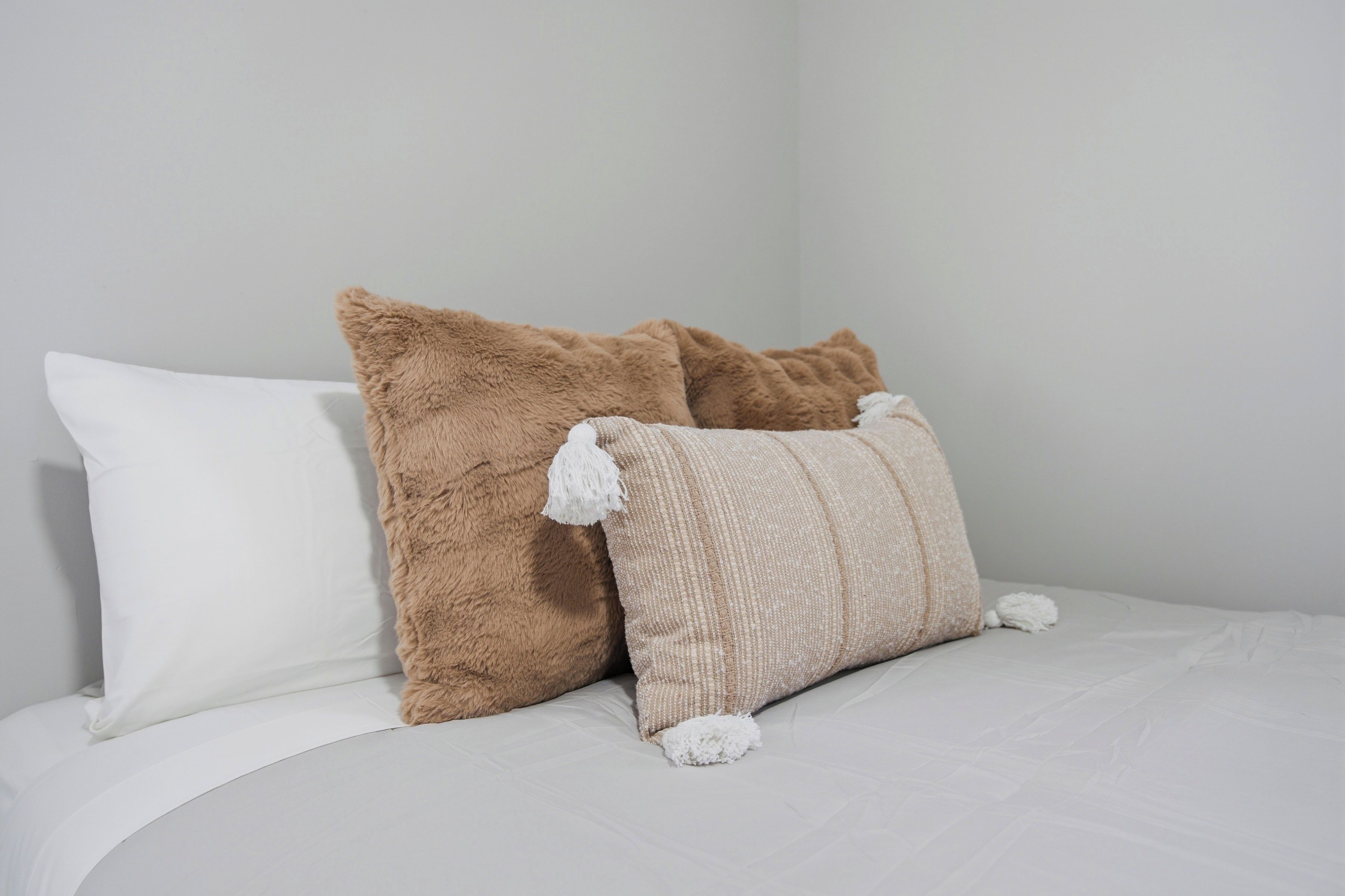 A bed with white bedding and two brown pillows.