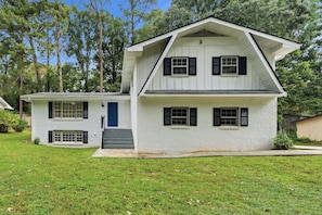 A two-story house with a front porch, a blue door, and a small front yard. - Spacious 5BR Home, Sleeps 12 | Near I-20 & I-285 (Decatur)
