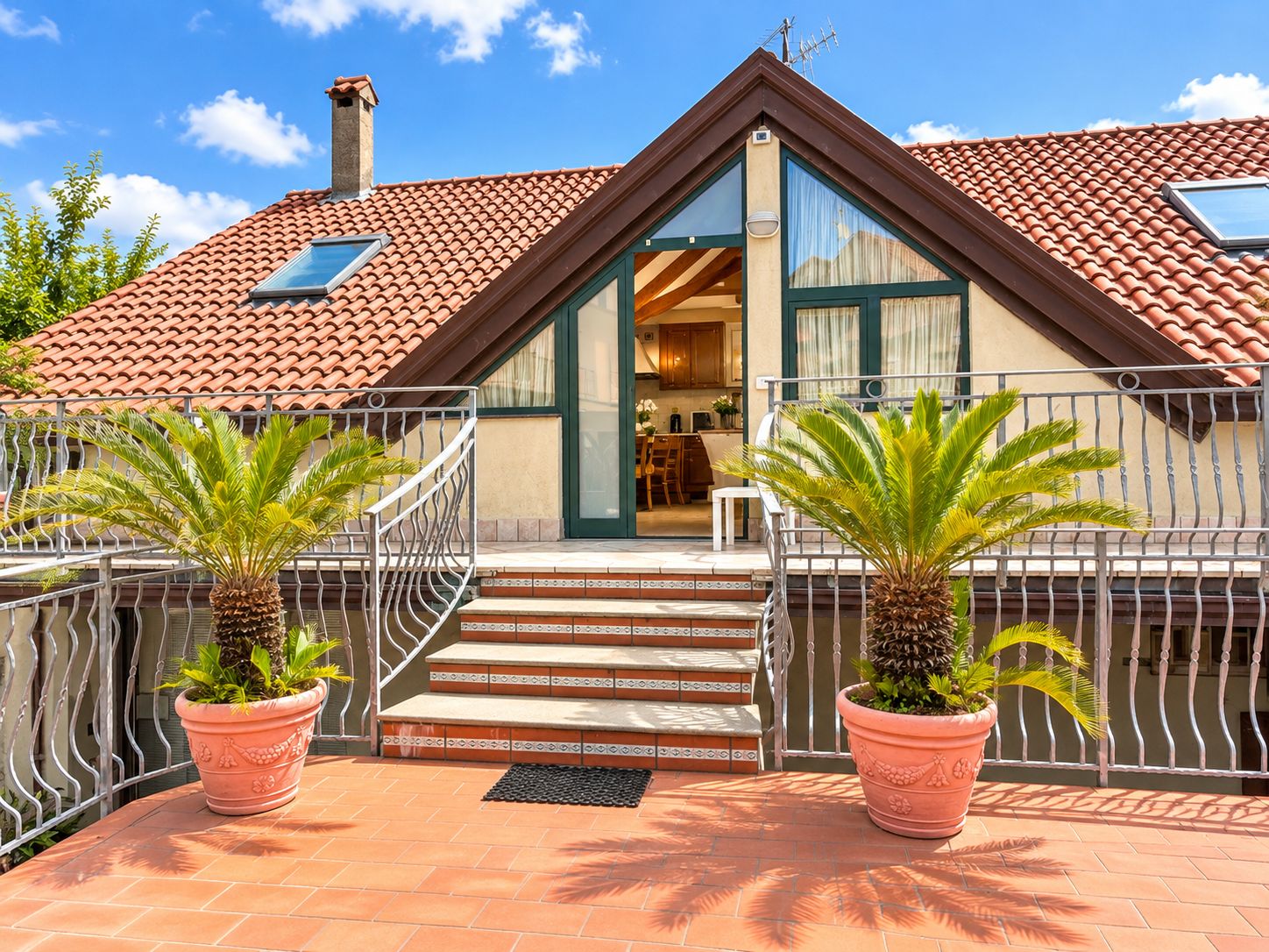 A two-story building with a red-tiled roof, a balcony with metal railings, and potted plants.