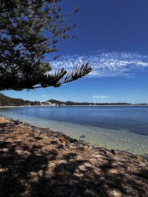 A clear coastal view with a tree in the foreground, a calm sea, and a distant shoreline with buildings. - Kingsview Shoal Bay - Water views, newly renovated (Shoal Bay)