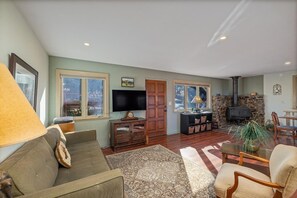 A living room with a sofa, armchairs, a TV, a fireplace, and a stone wall. - Your Yosemite Basecamp with Amazing Deck Views just south of Yosemite Entrance (Oakhurst)