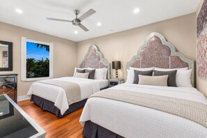 A bedroom with two beds, a ceiling fan, a nightstand, and a window with a view of greenery. - Casita Palma: Tiki Bar and Pickleball (Imperial Beach)