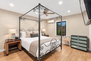 A four-poster bed with a ceiling fan, bedside lamps, a wooden floor, a window with a view, and a dresser with drawers. - Casita Palma: Tiki Bar and Pickleball (Imperial Beach)