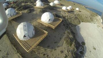 A series of dome-shaped structures with wooden walkways, set on a sandy terrain with a view of the sea.