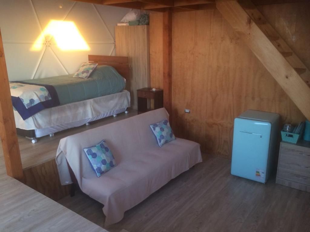 A room with a bed, a sofa, a small table, and a refrigerator.