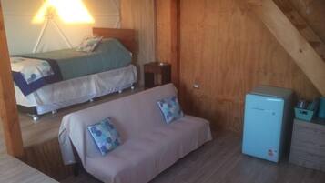 A room with a bed, a sofa, a small table, and a refrigerator.
