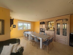 Un espace repas comprenant une longue table et des chaises, un buffet avec des portes en verre et un canapé.