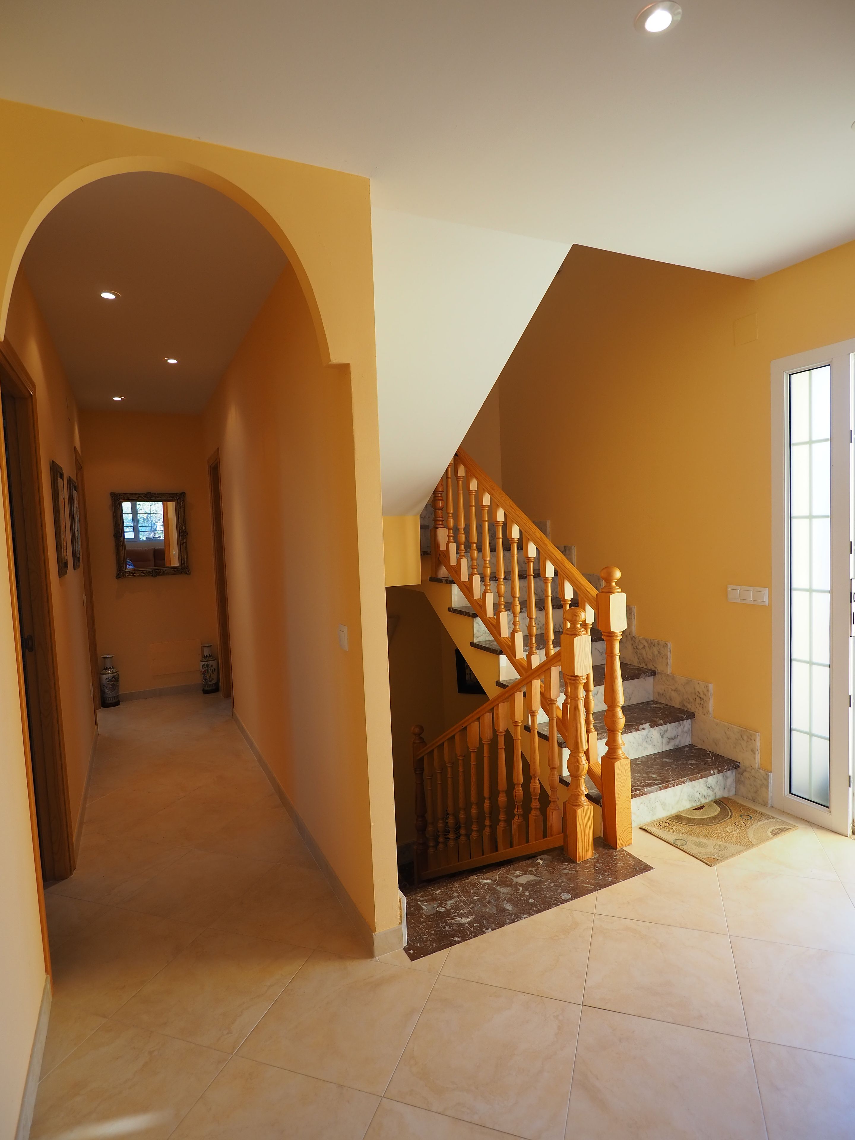 Un pasillo que conduce a una escalera con barandilla de madera y escalones de mármol.