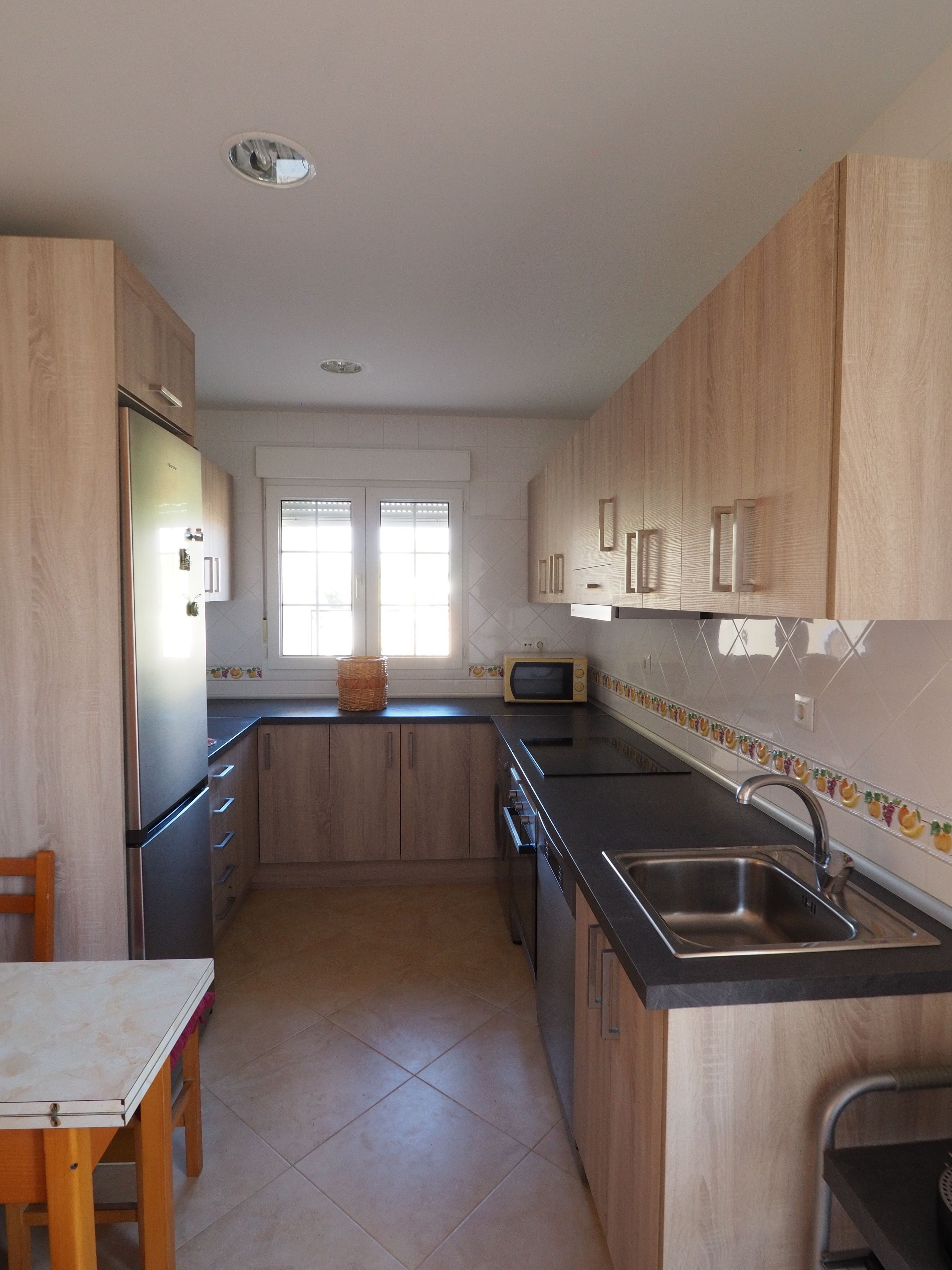 Una cocina con armarios de madera, un lavamanos de acero inoxidable, un microondas y una mesa de comedor con sillas.