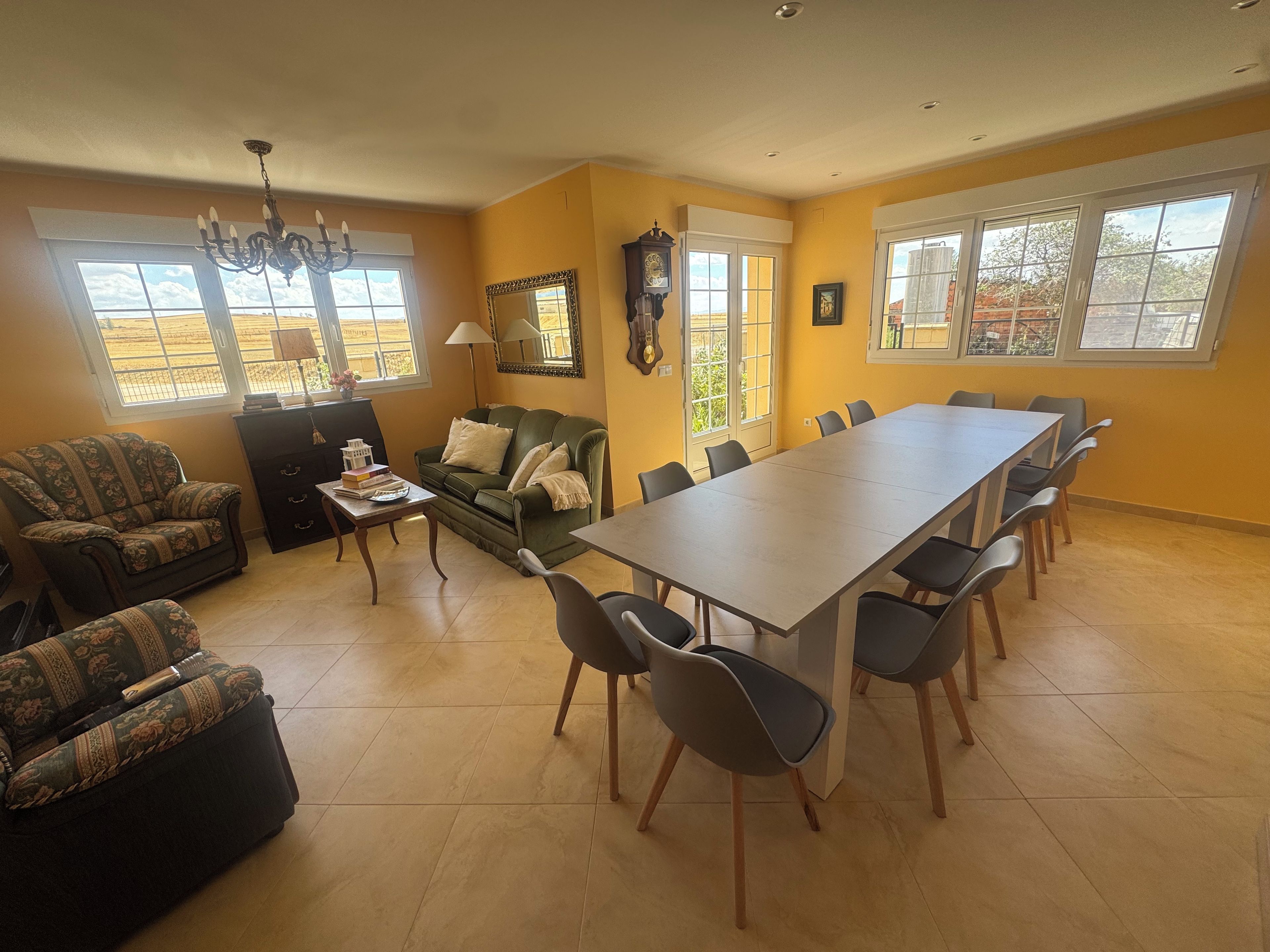 Un comedor con una mesa larga y sillas, un sofá, una lámpara y un reloj en la pared.
