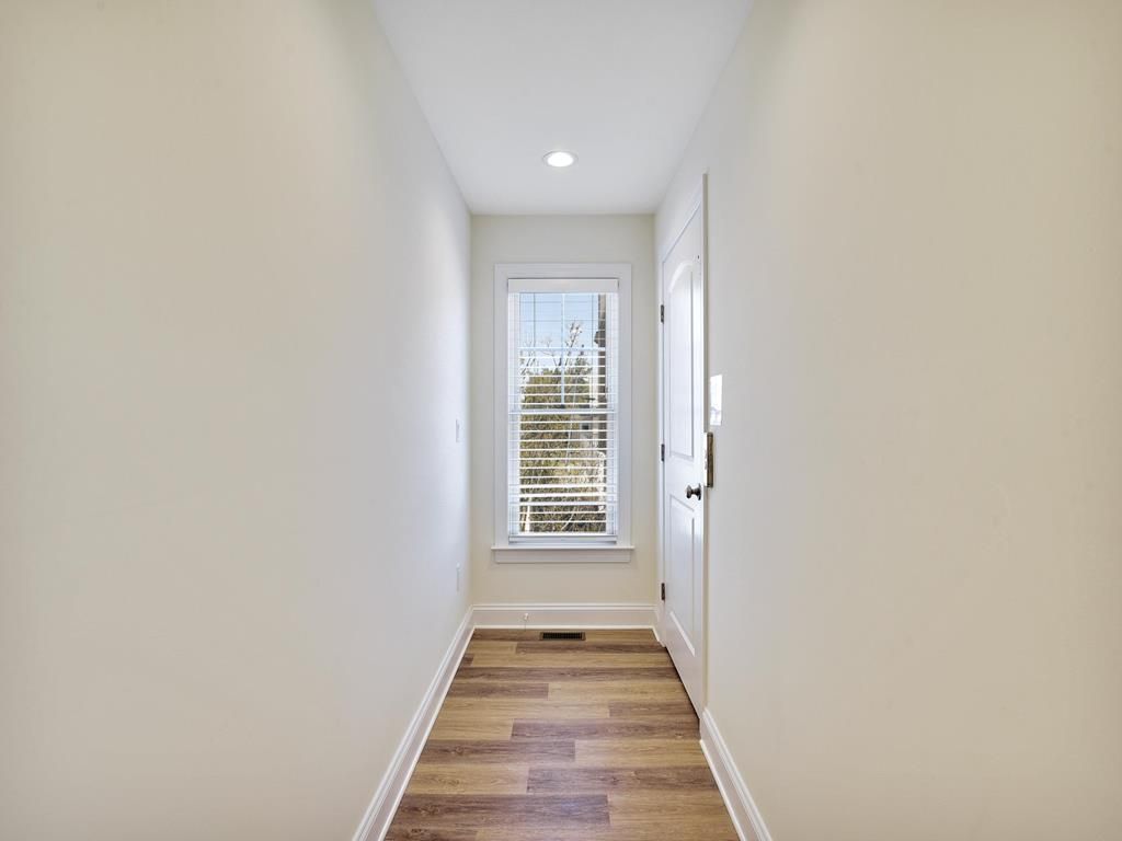 Un estrecho pasillo con suelo de madera, paredes blancas y una ventana con persianas.