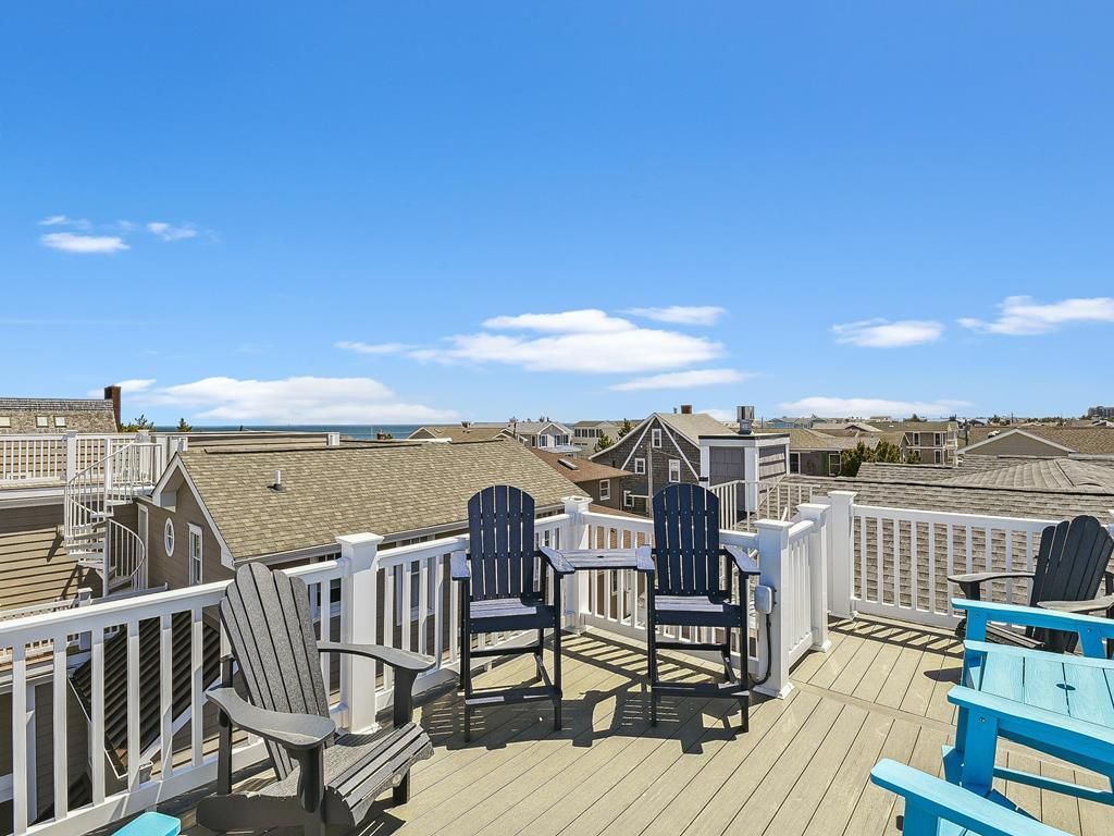 Eine Terrasse mit Adirondack-Stühlen und einer blauen Bank, mit Blick auf eine Küstenlandschaft mit Häusern.