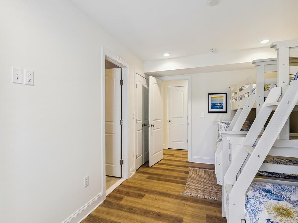 A hallway with wooden flooring, white walls, and a white staircase leading to a bedroom.