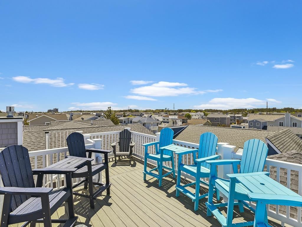 A deck with chairs and a table, overlooking a residential area with houses and a clear sky.