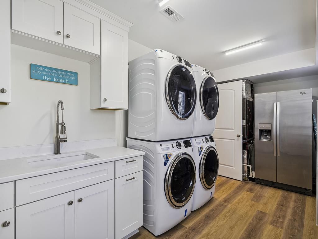 A laundry room with stacked front-loading washers and dryers, a stainless steel refrigerator, and a sink with a faucet.