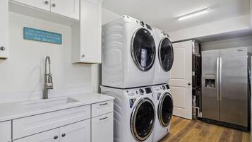 A laundry room with stacked front-loading washers and dryers, a stainless steel refrigerator, and a sink with a faucet.