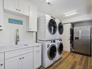 A laundry room with stacked front-loading washers and dryers, a stainless steel refrigerator, and a sink with a faucet. - Beachside Luxury | Spacious 7BR + Porch + Parking! (Bethany Beach)