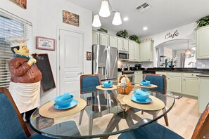A modern kitchen with a dining area, featuring a stainless steel refrigerator, microwave, and a glass dining table with blue bowls. - Chic 6BR, Pool, Themed Rooms, Near Disney (Kissimmee)