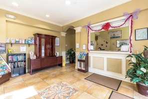 A reception area with a wooden desk, a bulletin board with various notices, a potted plant, and a tiled floor. - Chic 6BR, Pool, Themed Rooms, Near Disney (Kissimmee)